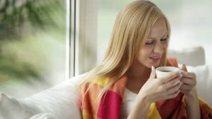 stock-footage-young-woman-sitting-on-sofa-drinking-tea-from-cup-looking-at-camera-and-smiling-panning-camera